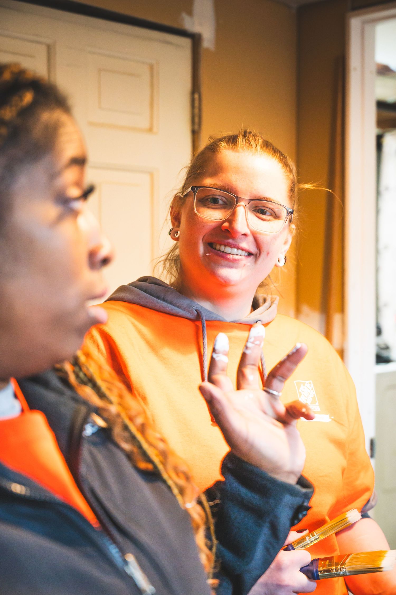 Two volunteers wearing orange hoodies share a lighthearted moment during a service project.