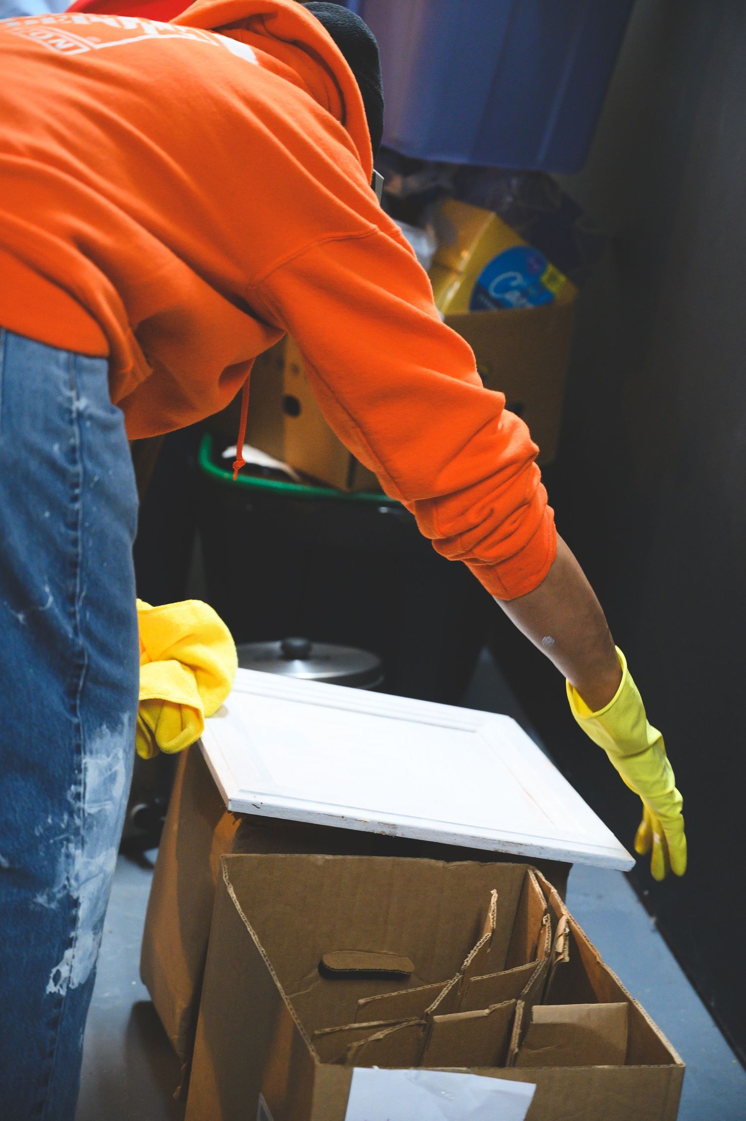 Volunteer in orange hoodie and yellow gloves reaches into cardboard boxes during a service project.