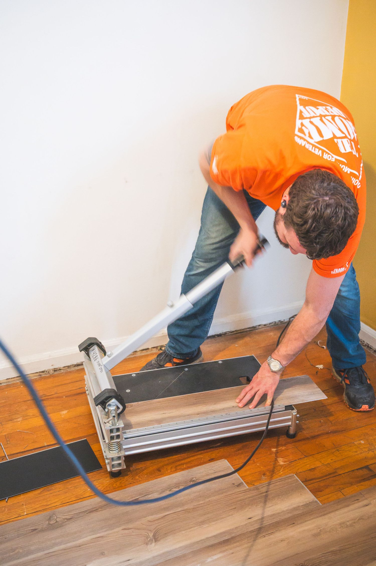 Person wearing orange Home Depot shirt operating flooring installation tool on hardwood floor.