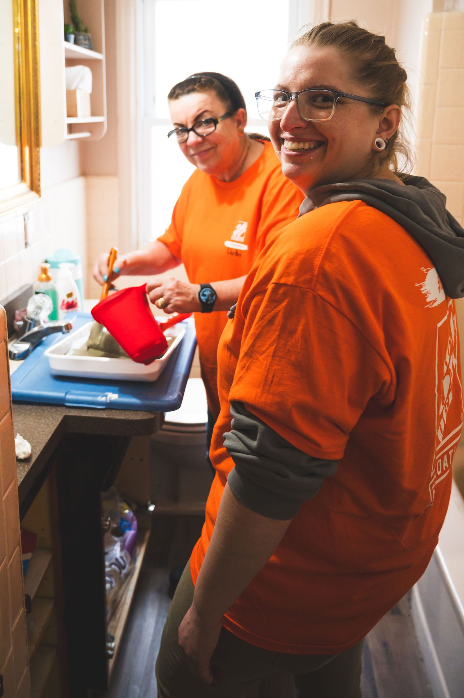 Two volunteers in orange shirts work together in a small kitchen space.