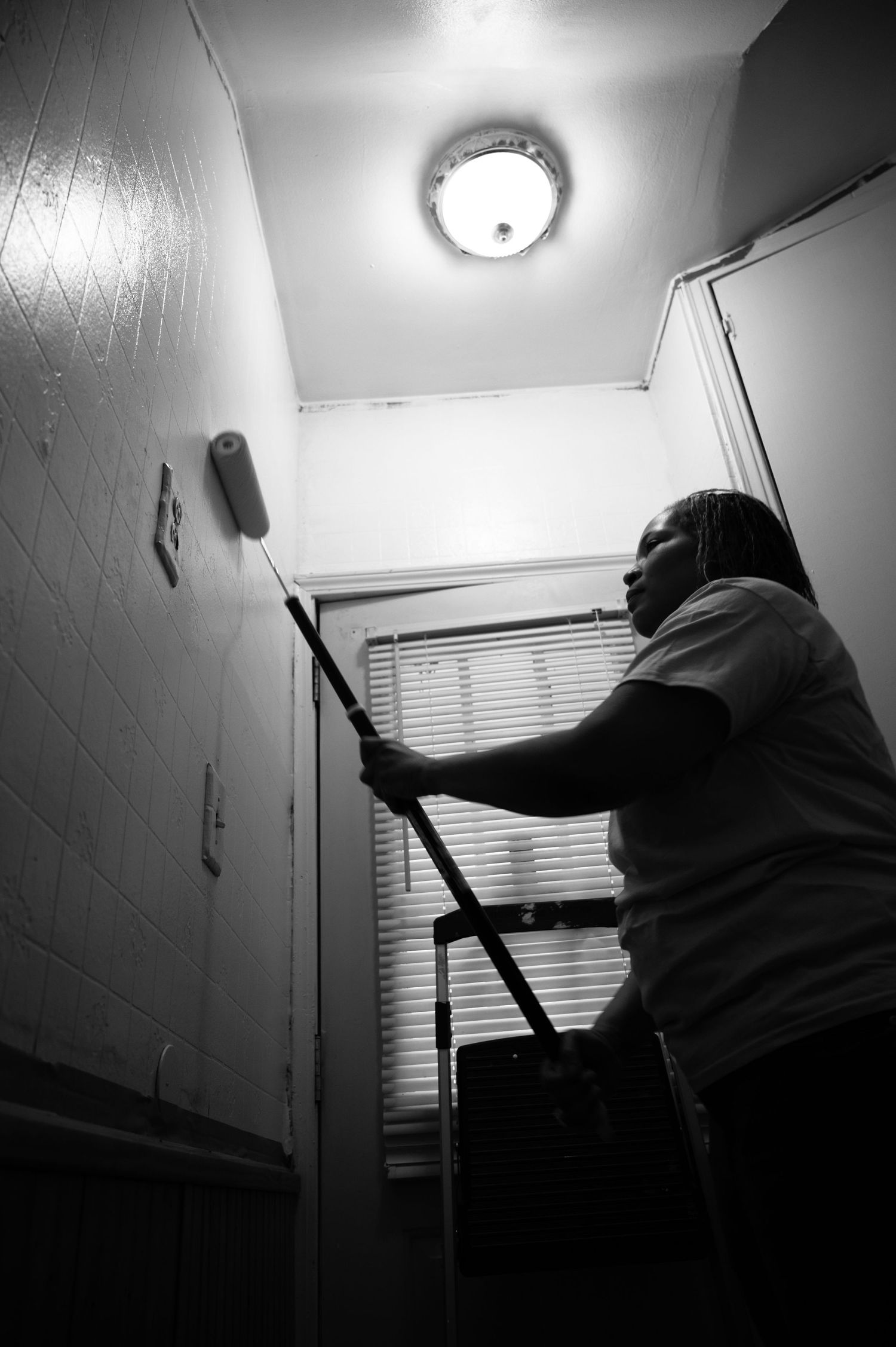 Silhouette of person mopping a hallway under ceiling light in dramatic black and white.