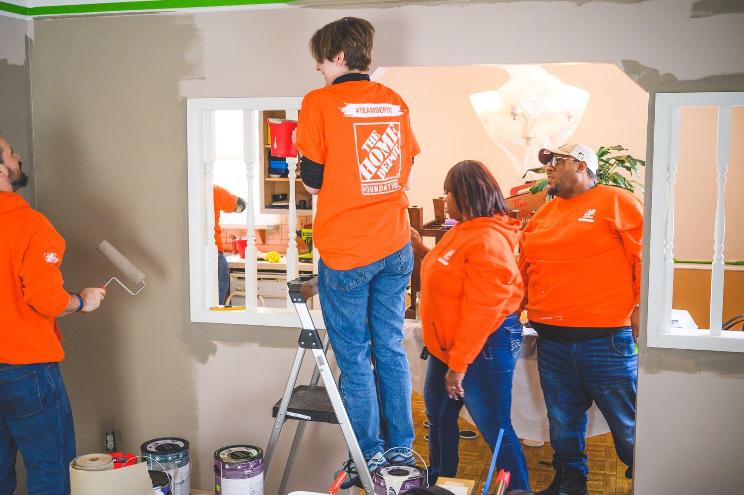 Group of volunteers in orange shirts painting interior walls together.
