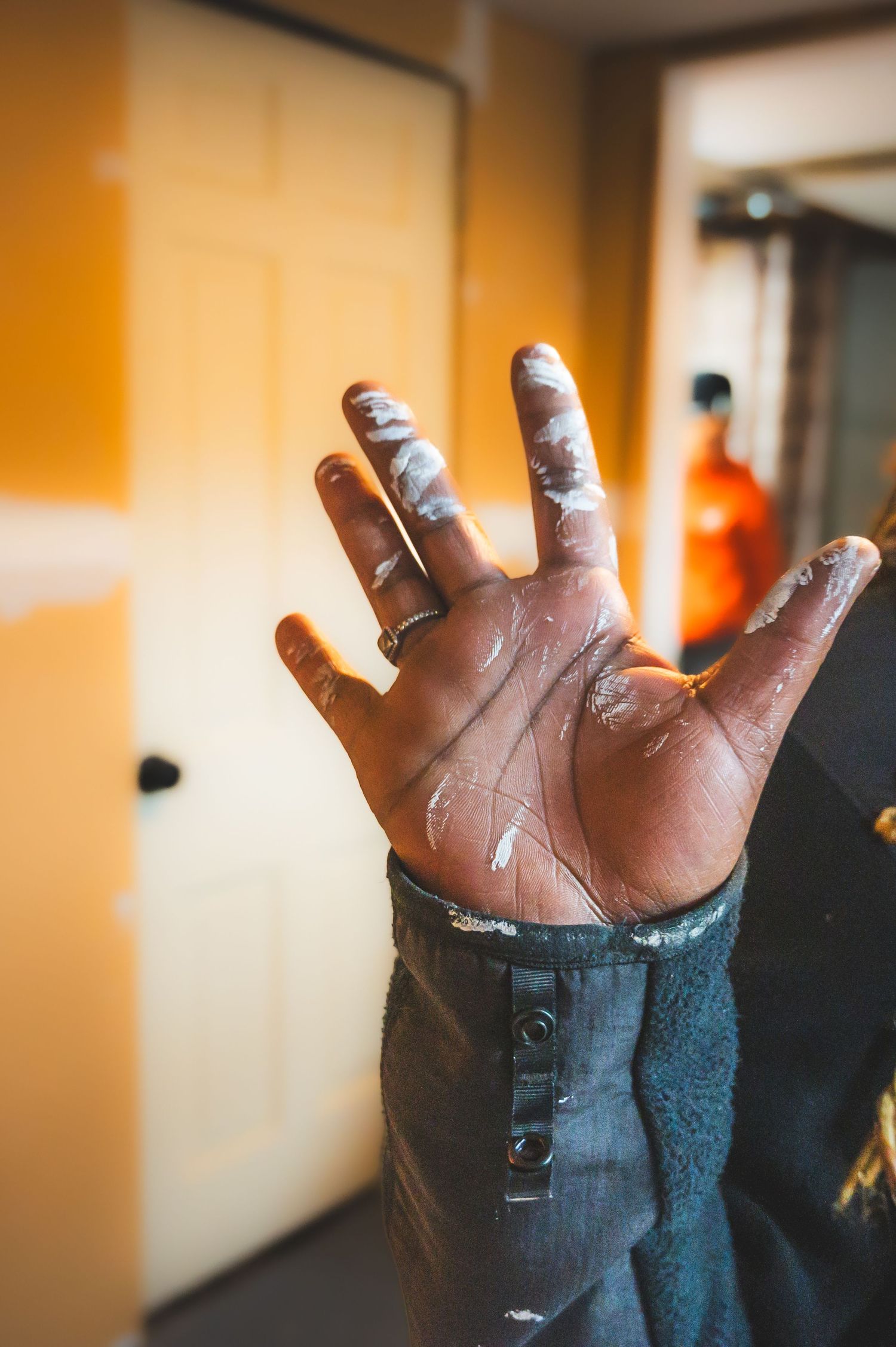 Close-up of paint-covered hand with wedding ring against orange background.