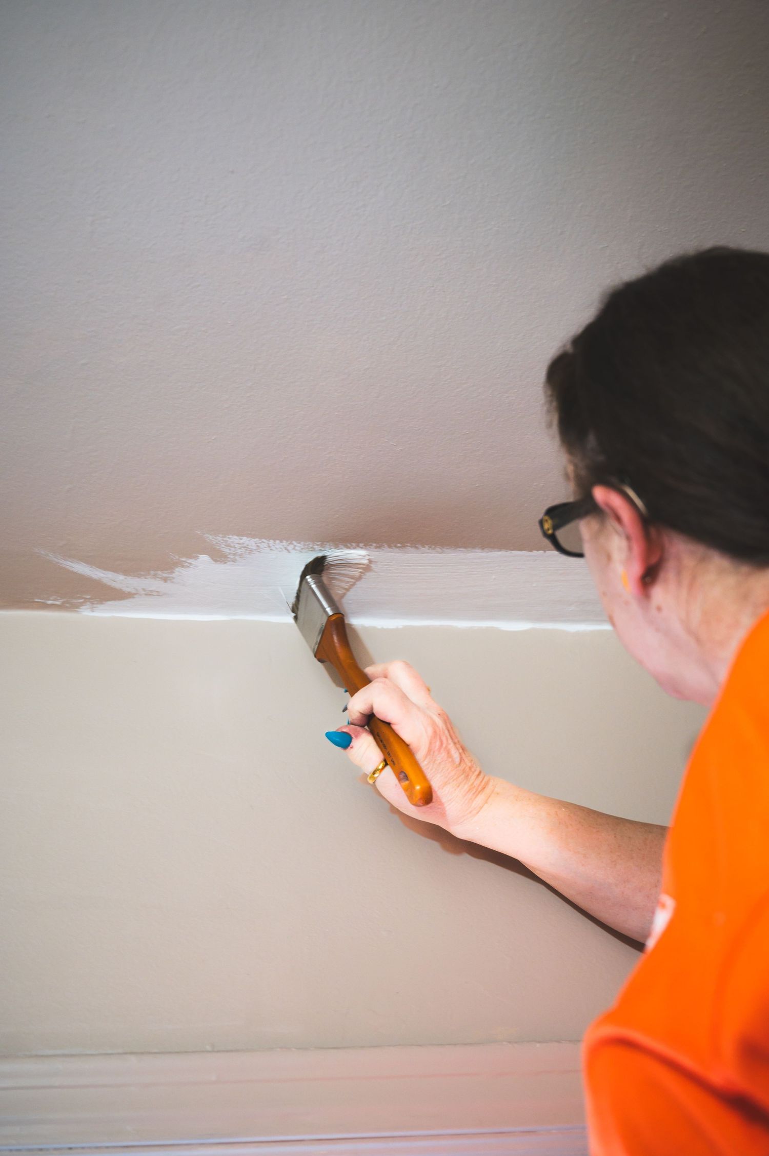 Person in orange shirt spackling a wall seam with putty knife during home improvement project.