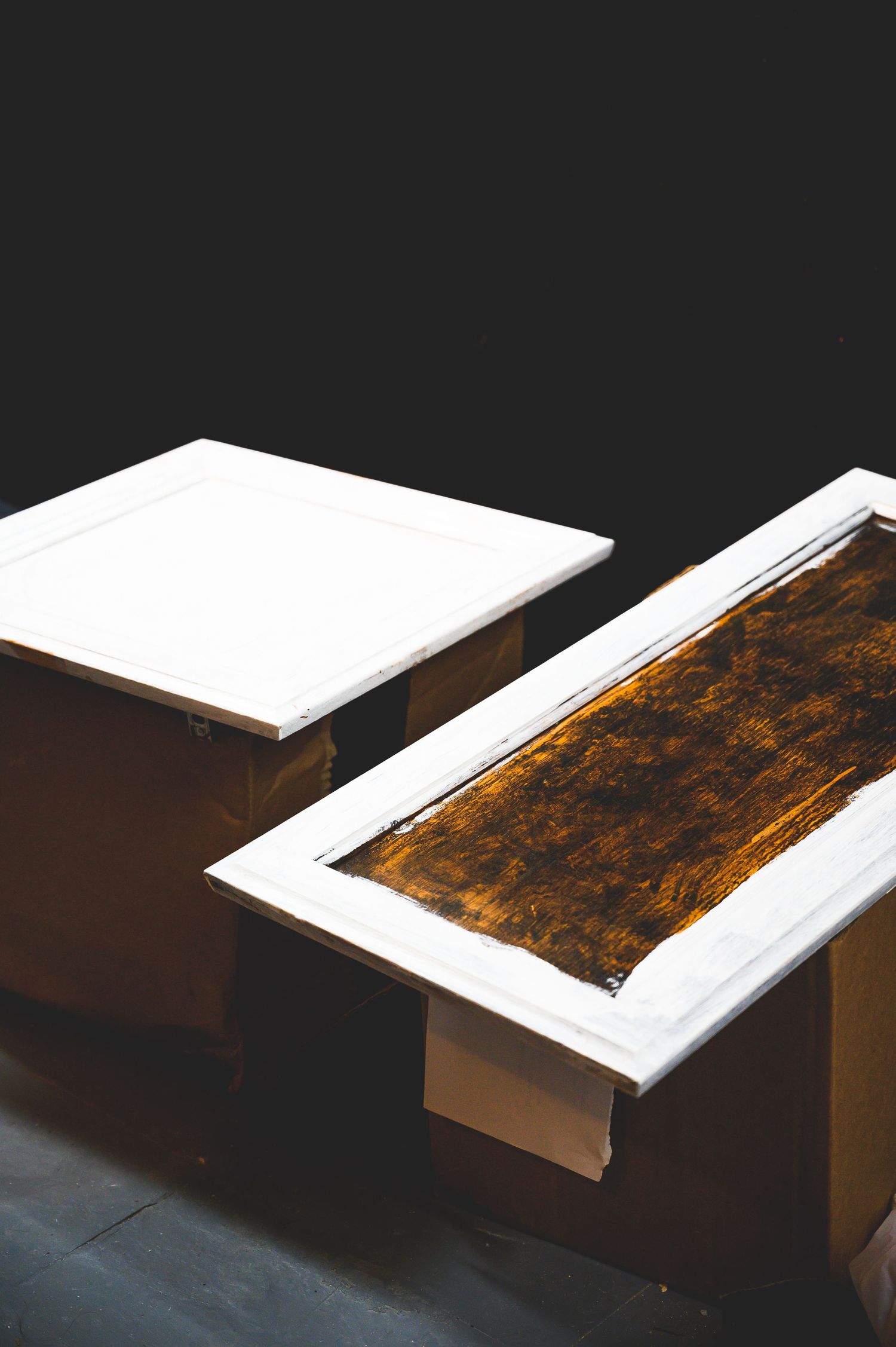 Two white and brown wooden frames on a dark surface against black background.