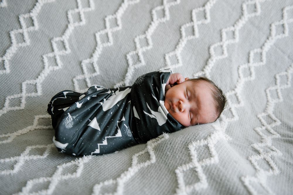 Newborn baby sleeping on white textured blanket in black and white swaddle.