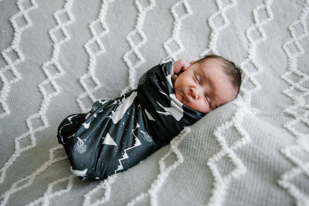 Newborn baby sleeping peacefully wrapped in patterned swaddle on textured white blanket.