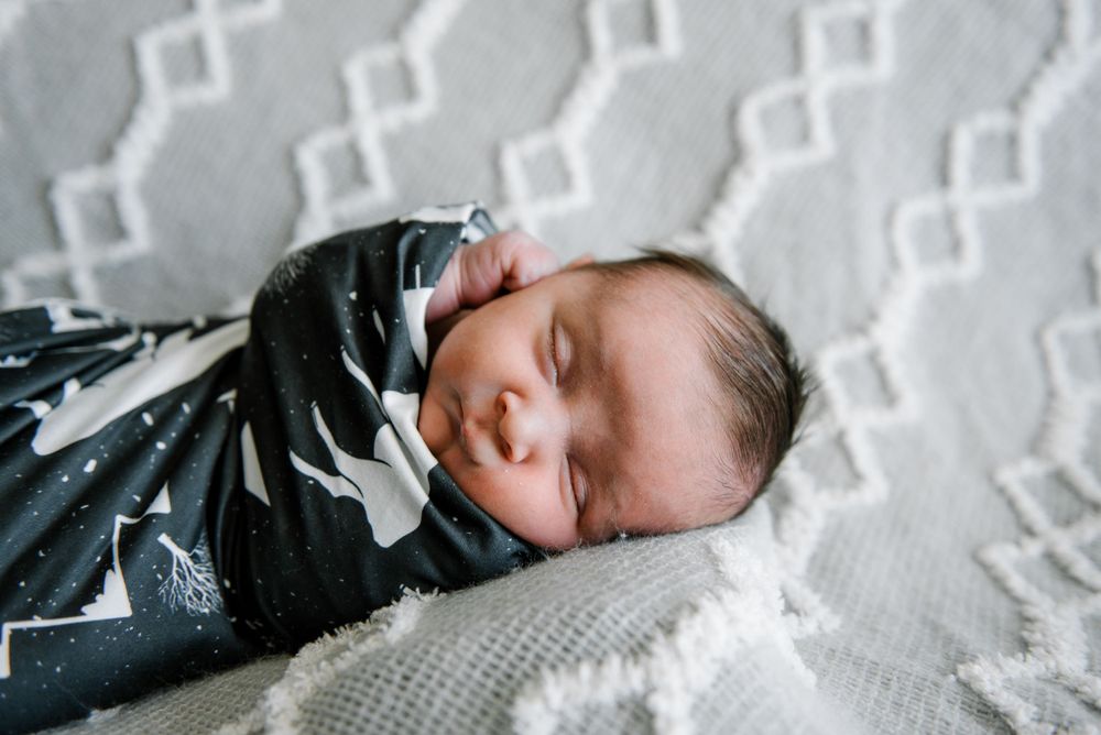 Sleeping newborn wrapped in black and white swaddle on textured blanket.