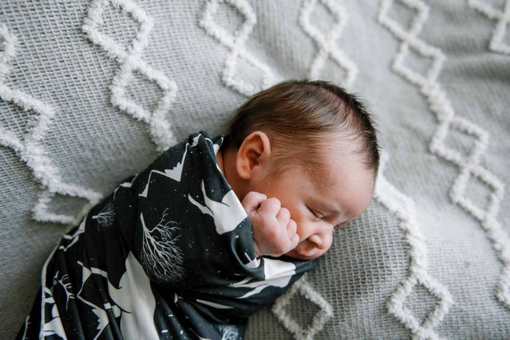 Sleeping newborn wrapped in patterned blanket on textured gray blanket.
