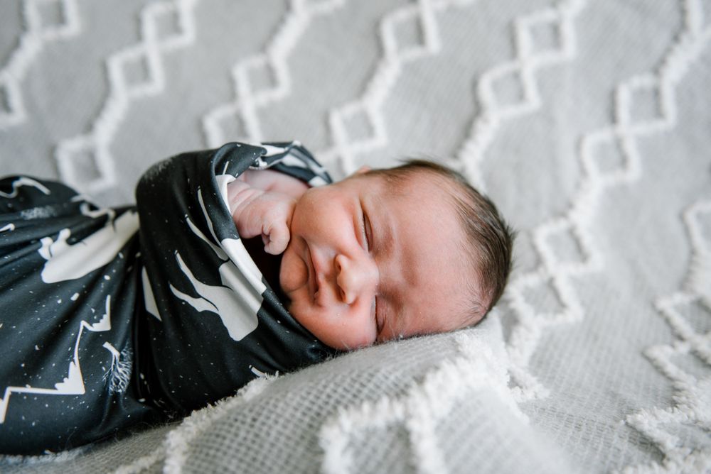 Peaceful newborn sleeps while swaddled in patterned wrap on white textured blanket.