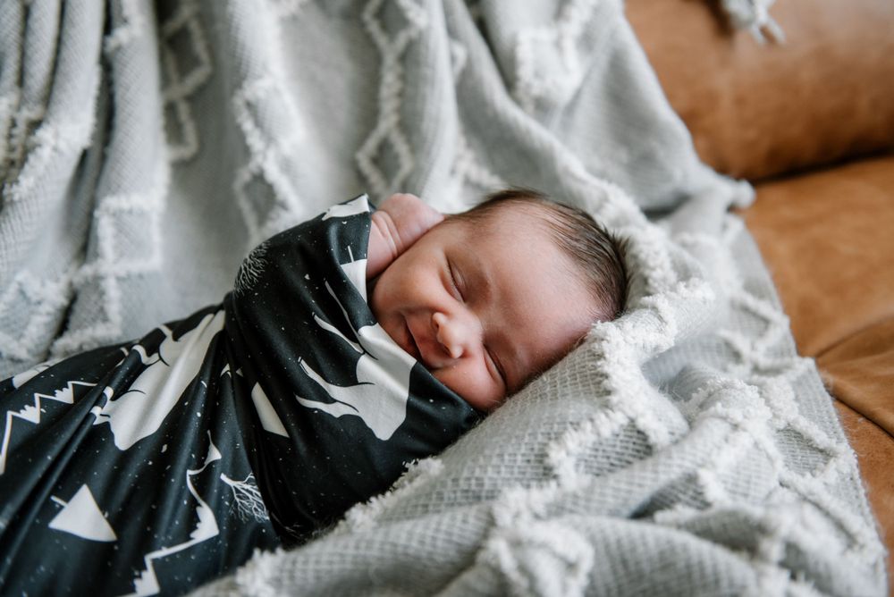 Baby sleeping peacefully on brown leather sofa with white textured blanket.