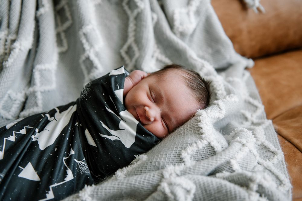 Infant resting on brown leather couch with white knitted throw.