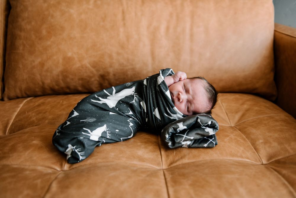 Sleeping infant in patterned onesie on tufted leather couch.