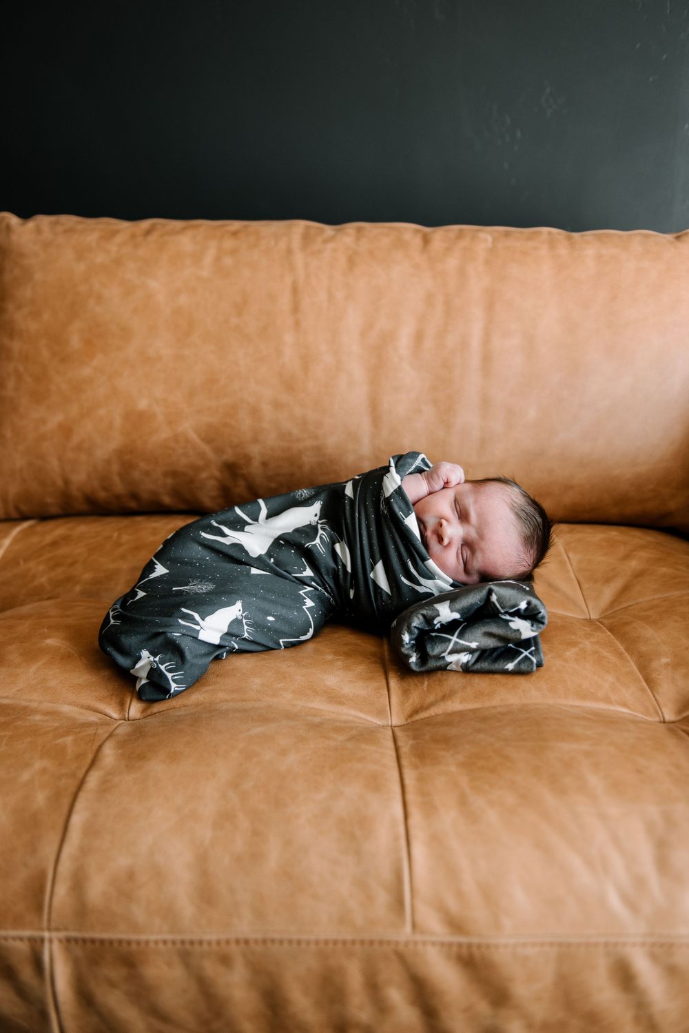 Baby in black and white patterned outfit sleeping on tan leather sofa.