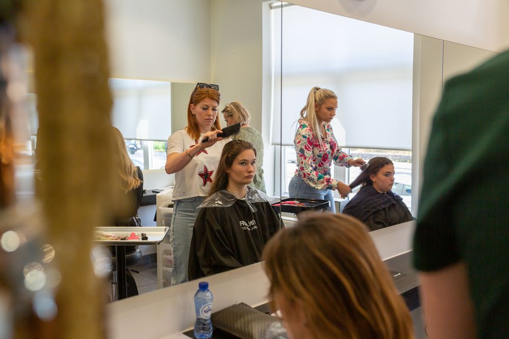 Hair stylists working on clients in a modern salon setting with bright natural lighting.