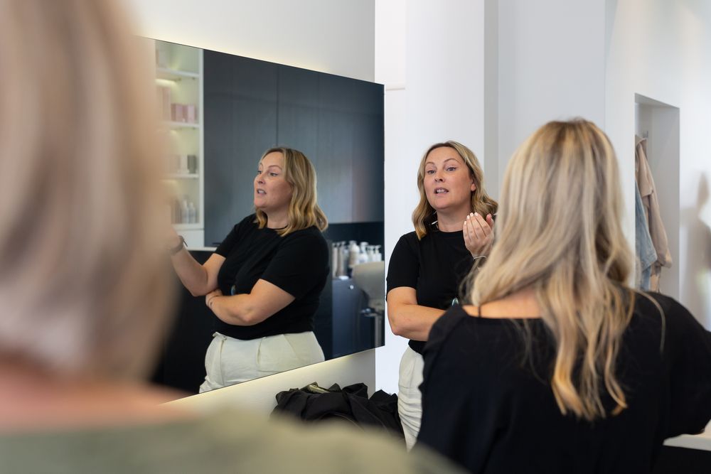 Professional hair stylists in black attire working in a modern salon with mirror reflections.