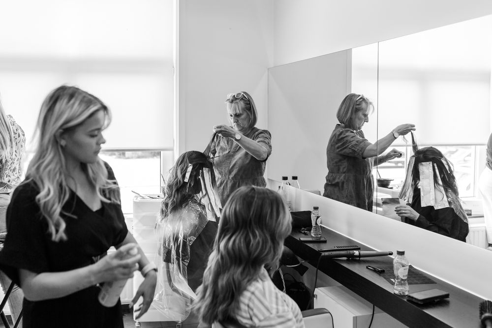 Black and white photo of a hair styling session in a brightly lit salon room.