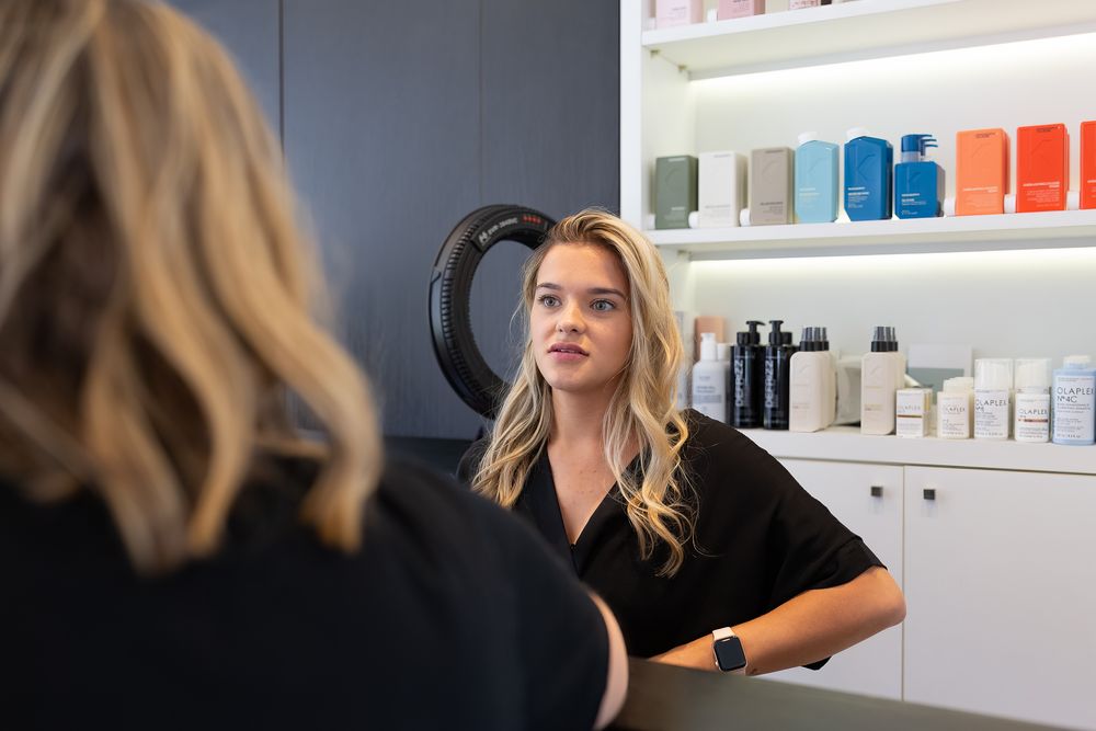 Professional hair salon interior with stylist consulting client near product display shelves.