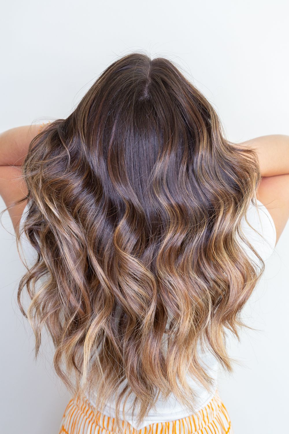 Back view of wavy balayage hair with brunette to caramel ombre transition.