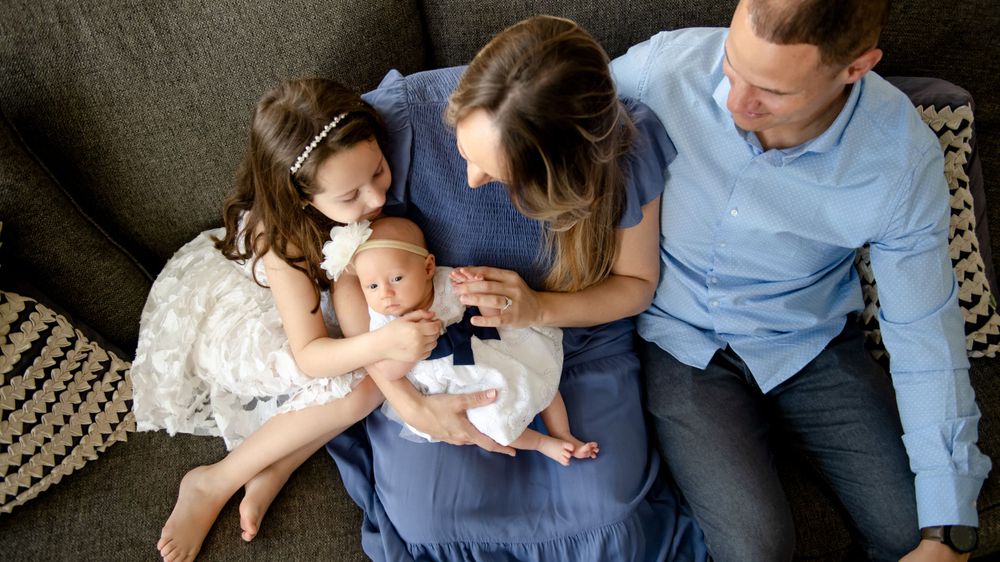 Family photo session on a grey couch showing loving interactions with a newborn baby.