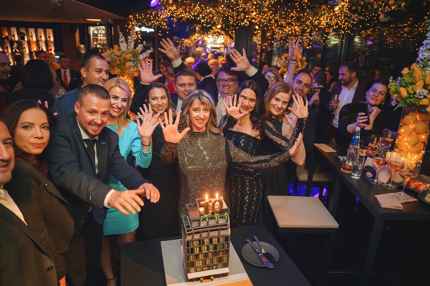 Lively celebration scene at night with party crowd and decorative lights.