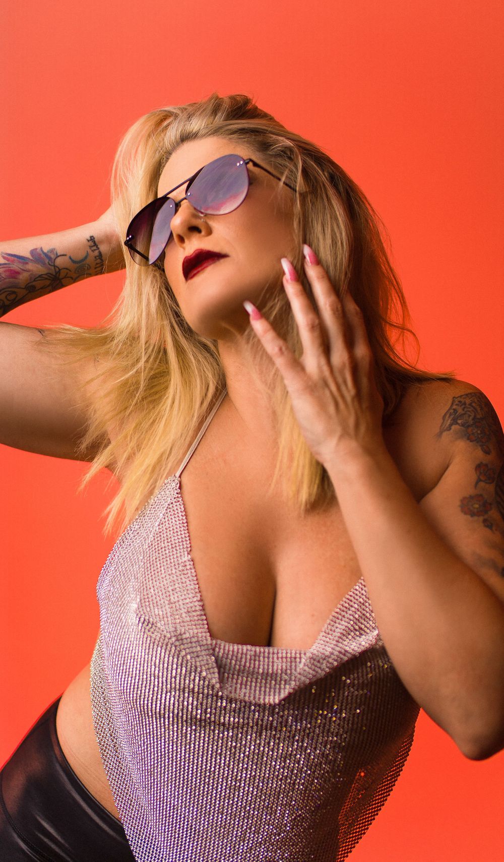 Glamour portrait against orange background featuring sparkly top and aviator sunglasses.