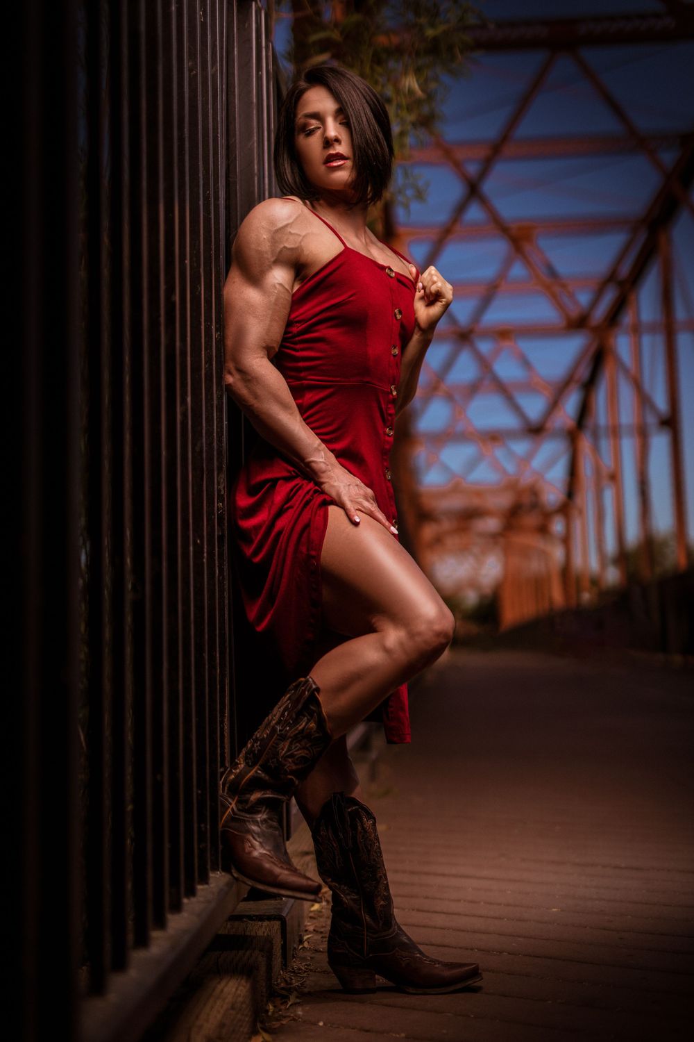 Athletic figure in red dress poses dramatically on rustic bridge structure.