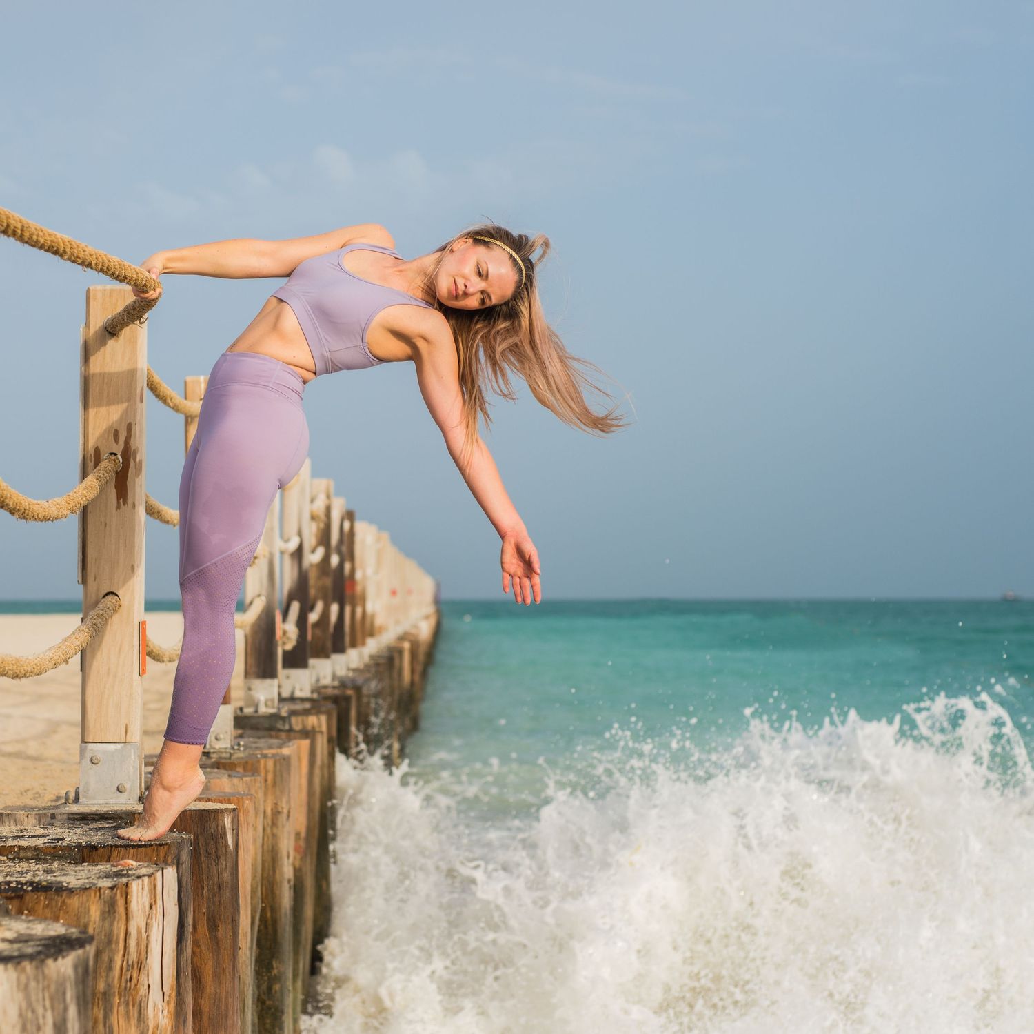 Yoga photography image taken on a beach in Dubai. Model is leaning out from a wall over the sea in a graceful pose.