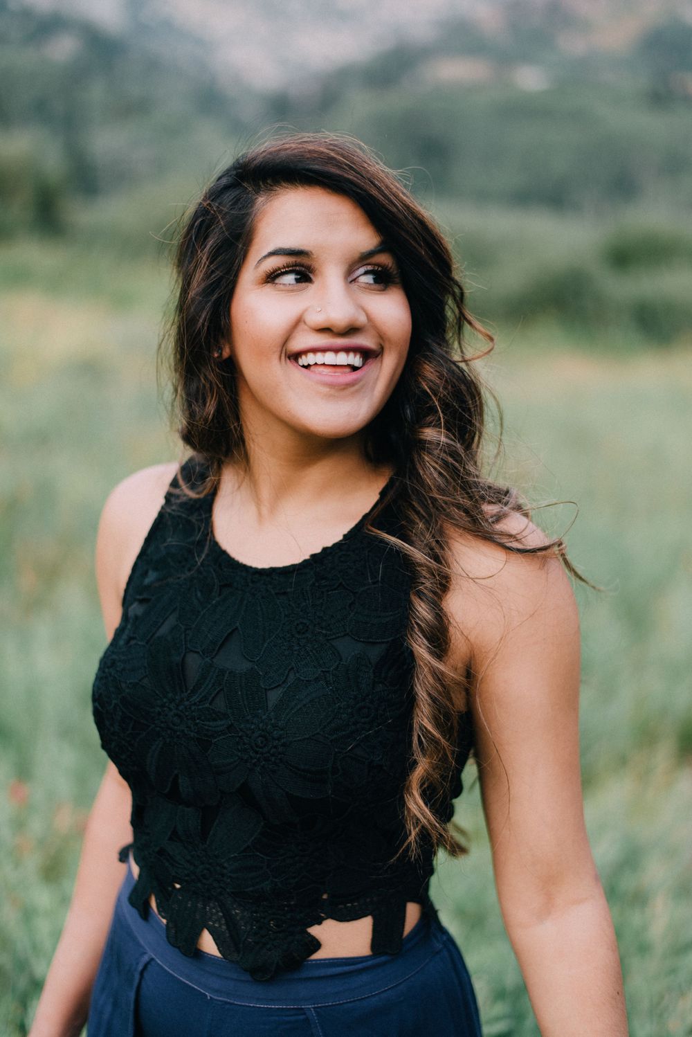 Woman in black top smiling during outdoor photoshoot with natural scenery.