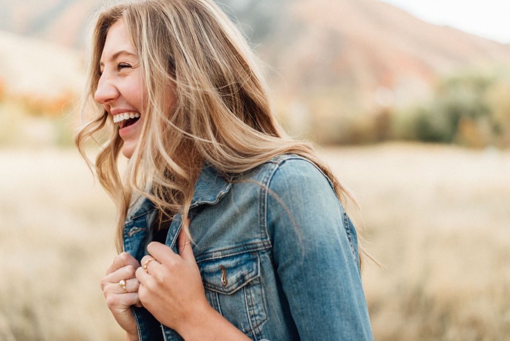 Woman in denim jacket smiling and laughing in warm outdoor setting with golden light.