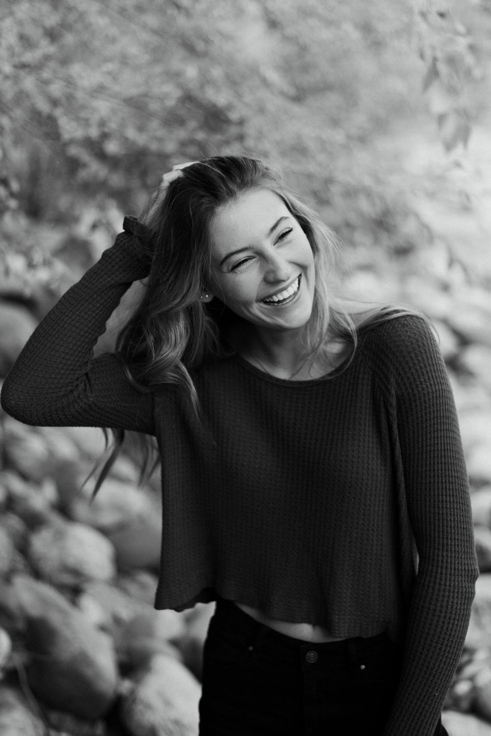 Black and white portrait of woman in sweater laughing against blurred natural background.
