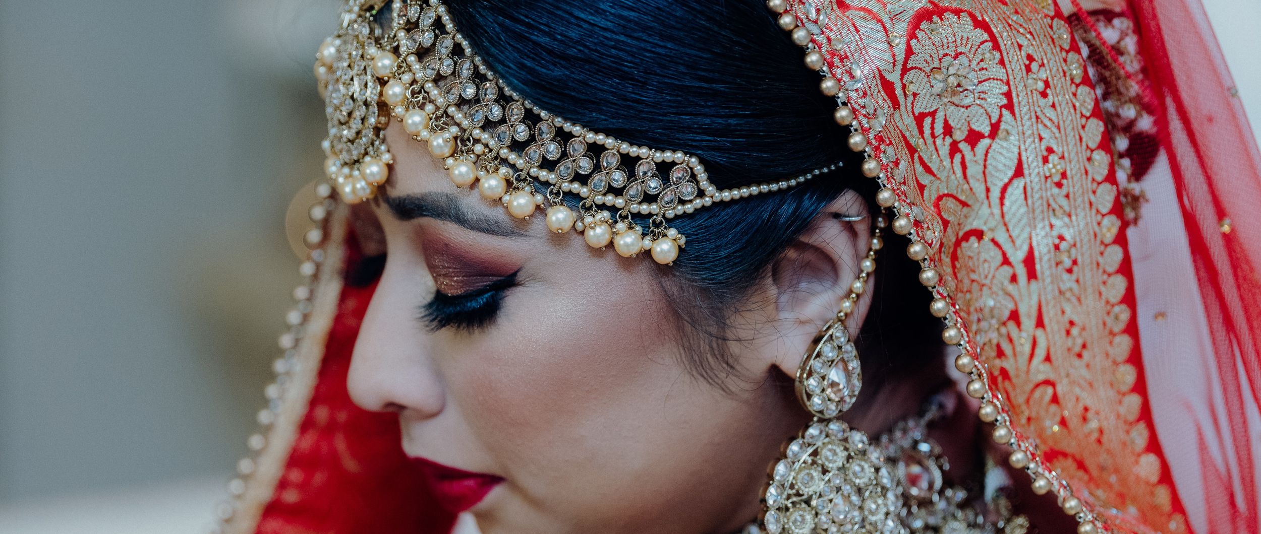 Side profile of bride in traditional Indian wedding attire with ornate jewelry and red veil.