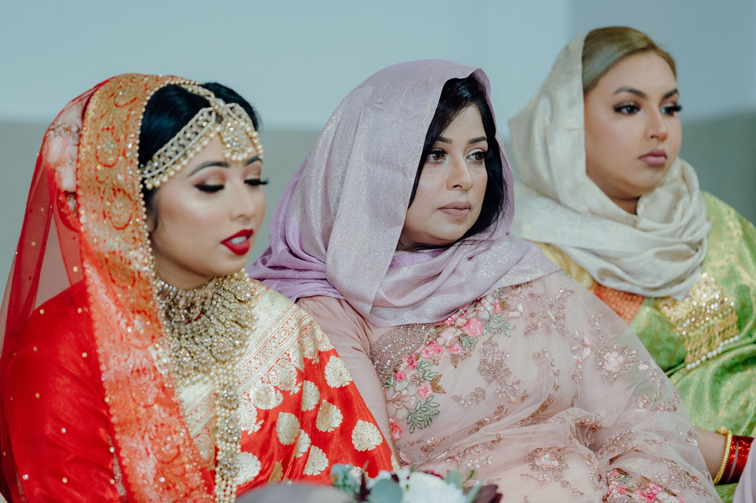 Three women wearing colorful traditional hijabs and formal attire sit together during a cultural celebration.