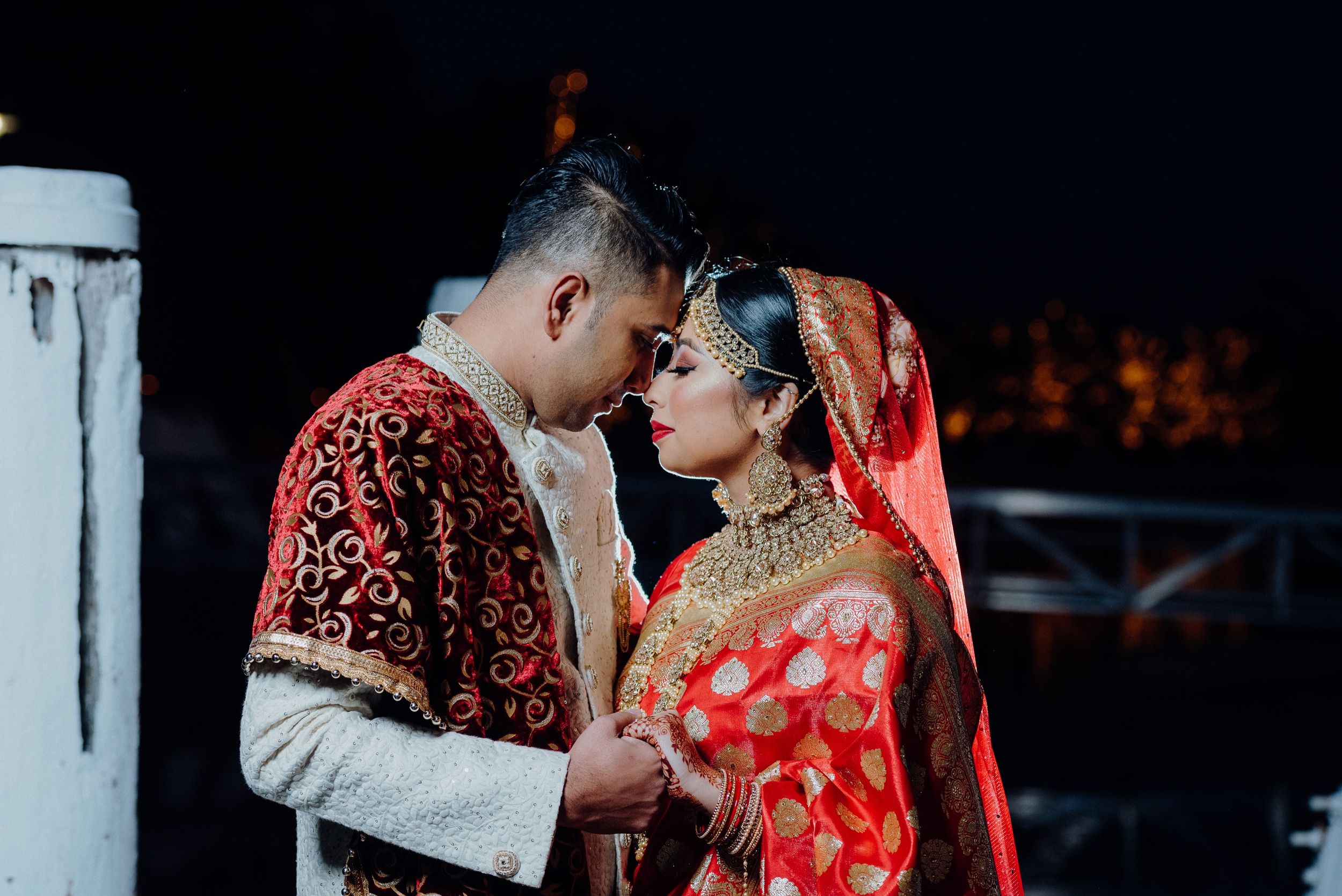 Intimate moment between couple in traditional South Asian wedding attire on wooden dock.