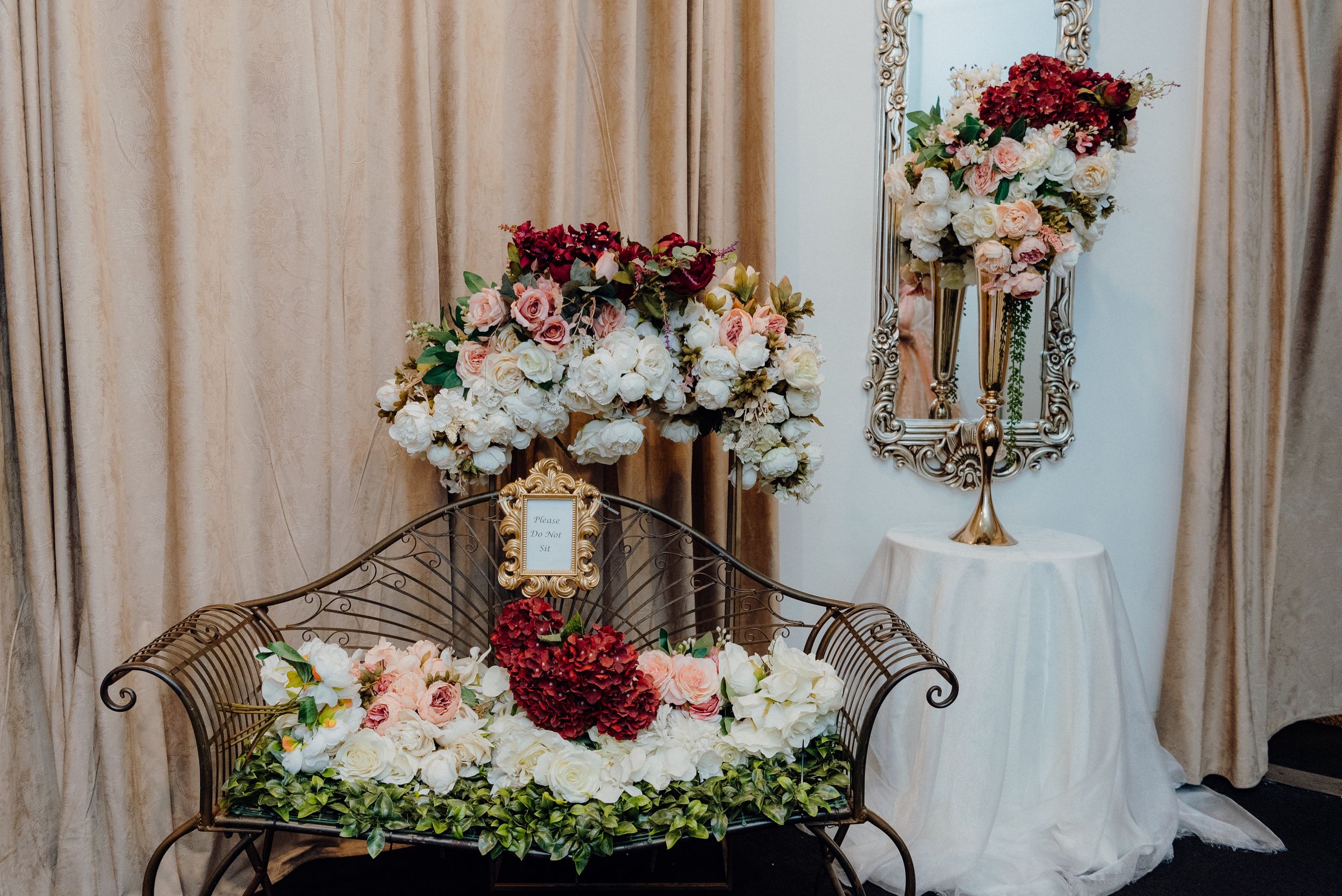 Romantic wedding decor featuring vintage settee with burgundy and white floral arrangements.