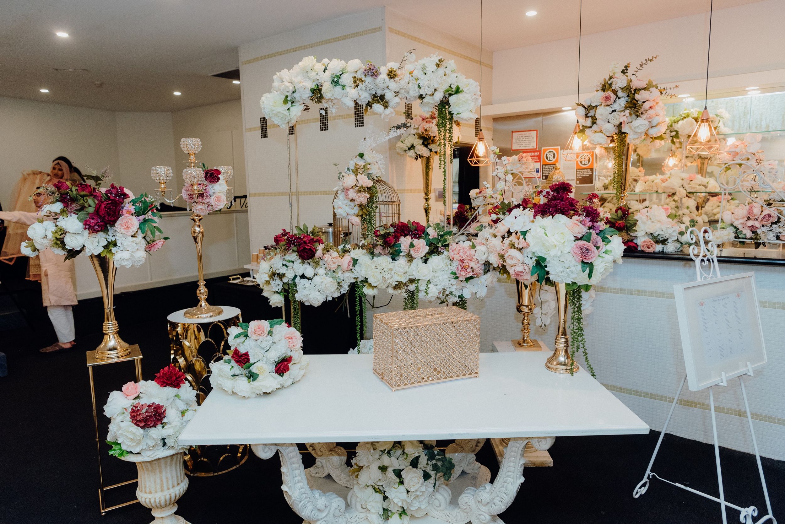 Modern wedding reception setup with white tables, floral centerpieces and hanging garden decorations.