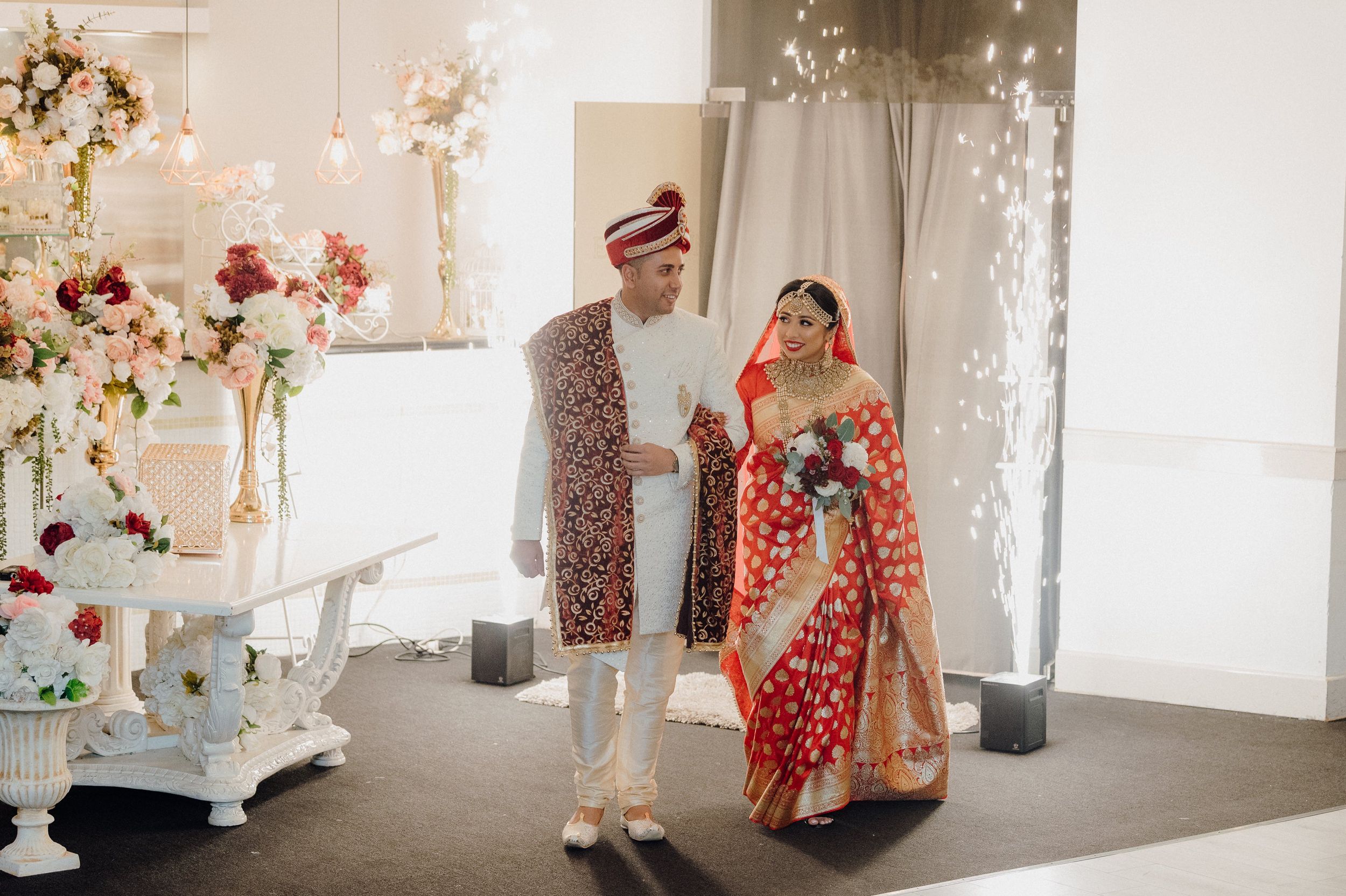 Wedding couple in traditional red and white attire dancing in an elegantly decorated reception hall.