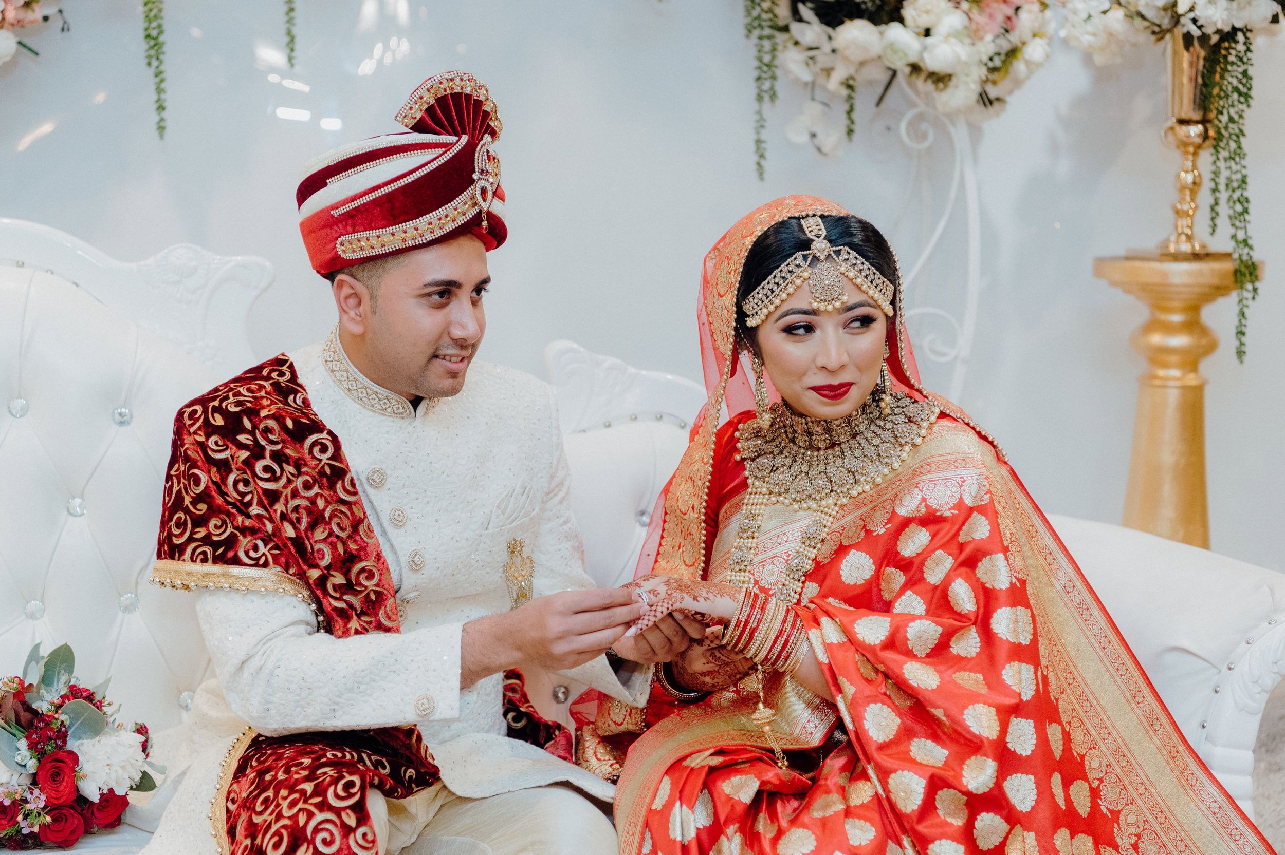 A couple in traditional red and white wedding attire performing ring exchange ritual.
