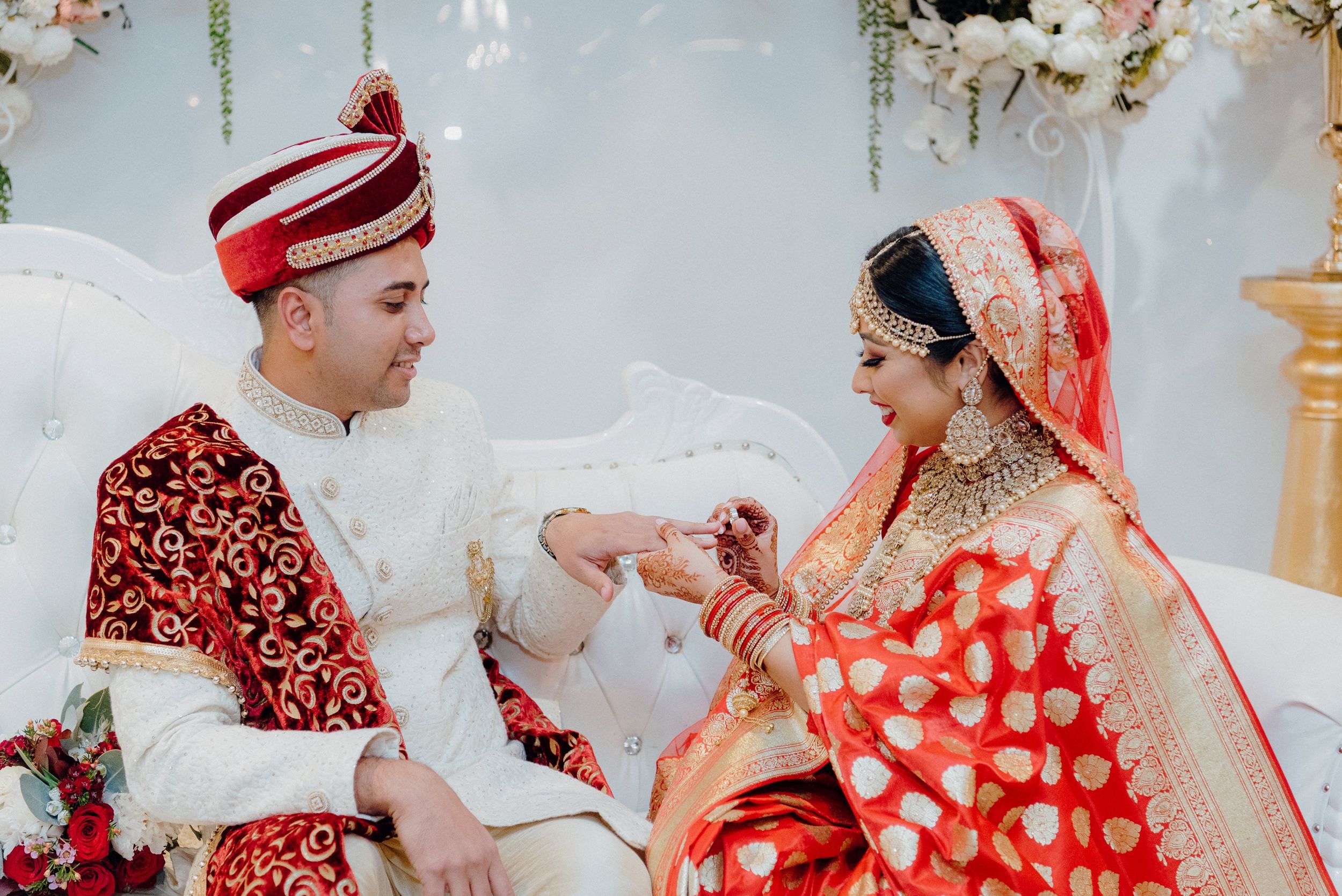 Traditional wedding ceremony with couple in red and white attire exchanging rings.