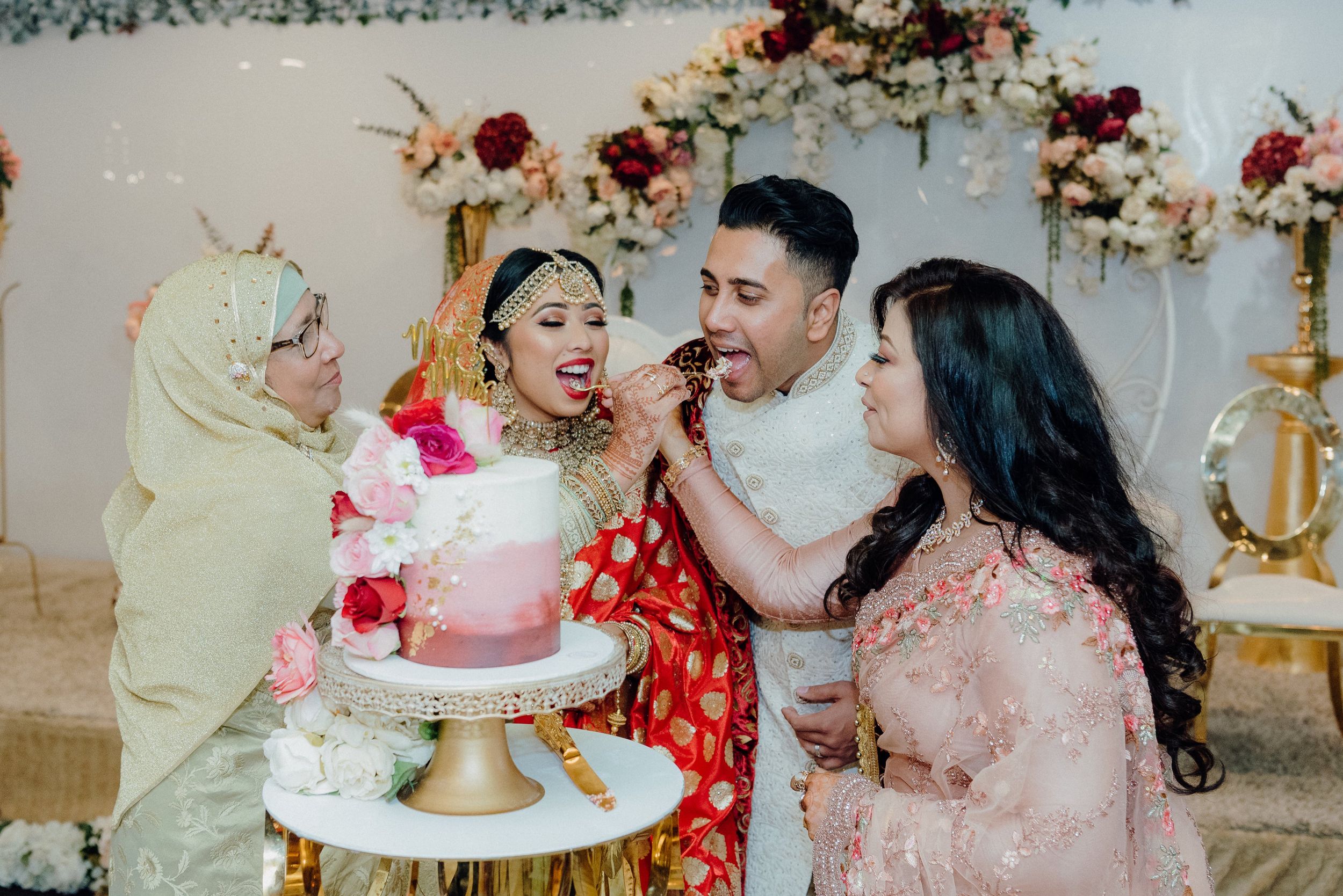 Joyful cake cutting moment during wedding reception with floral backdrop and gold details.