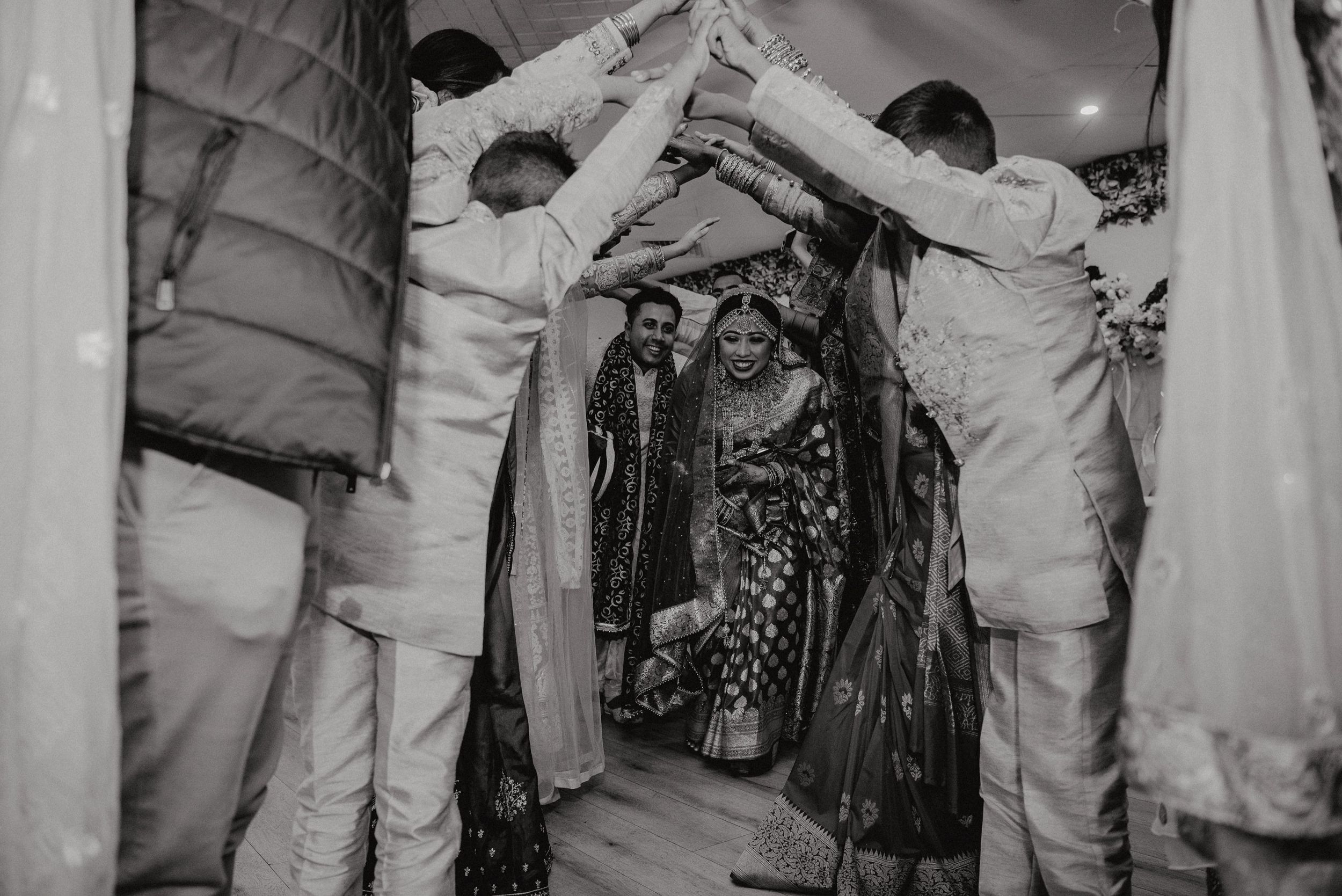 Black and white photo of guests forming a dance tunnel at a wedding celebration.