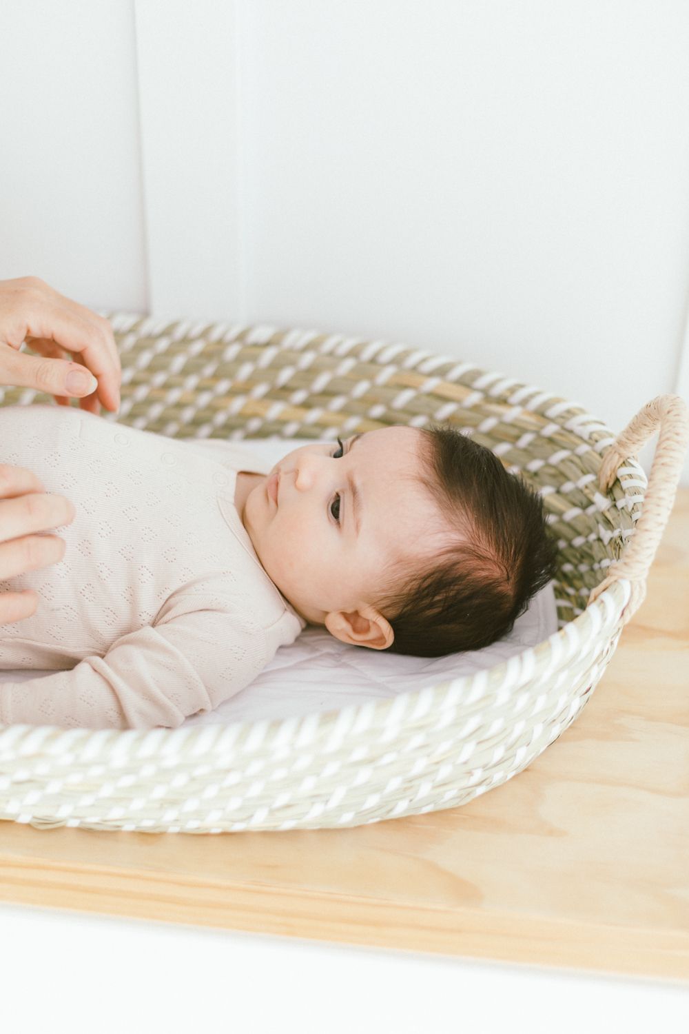 Baby lying on cream-colored woven mat in artistic natural light portrait series.