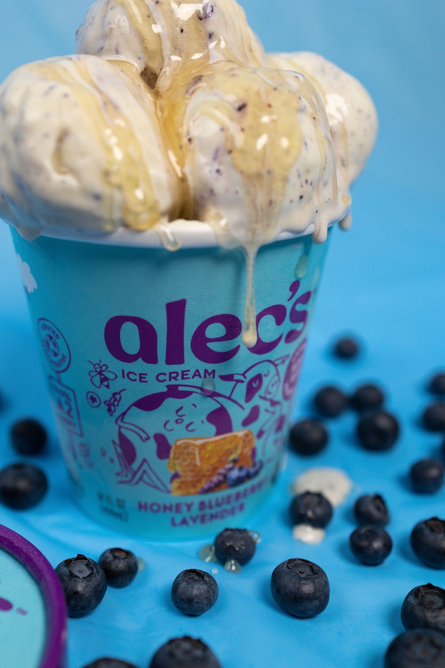 Alec's Honey Blueberry Lavender ice cream pint overflows with scoops surrounded by fresh blueberries.