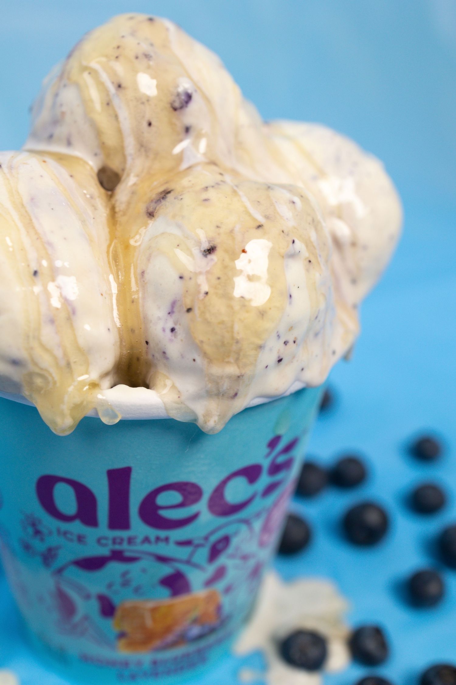 Close-up of Alec's Honey Blueberry Lavender ice cream scoops drizzled with honey beside fresh blueberries.