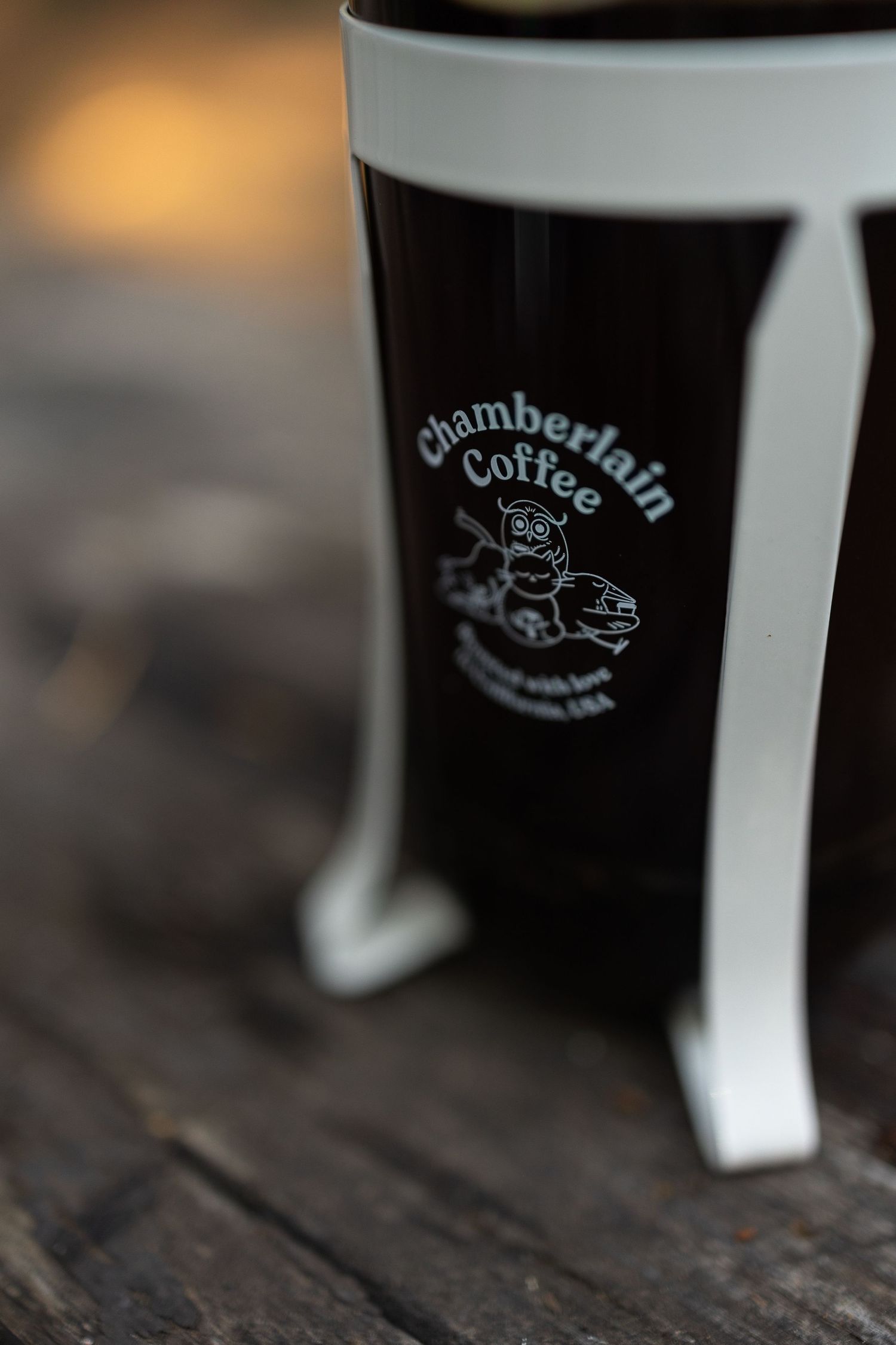 Close-up of Chamberlain Coffee branded French press with owl logo on dark glass cylinder.