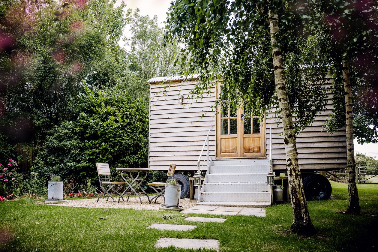 Charming white wooden cabin with a small porch and outdoor seating area in a garden setting.
