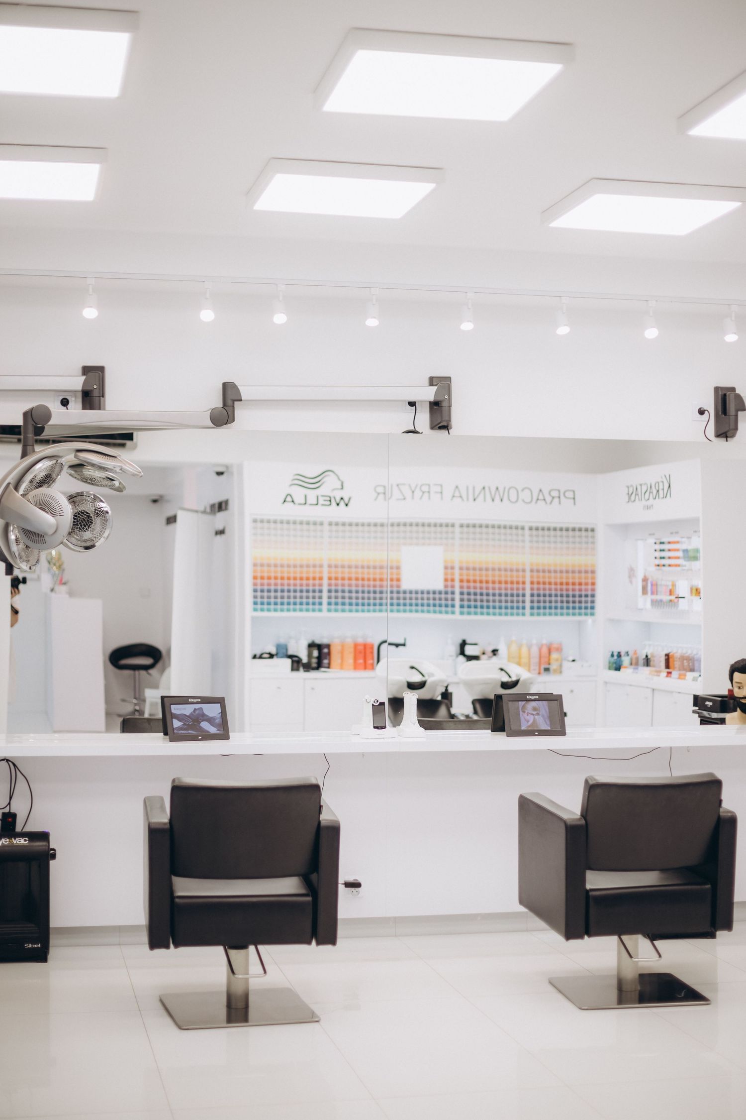 Modern minimalist salon interior with white decor and mounted styling equipment.
