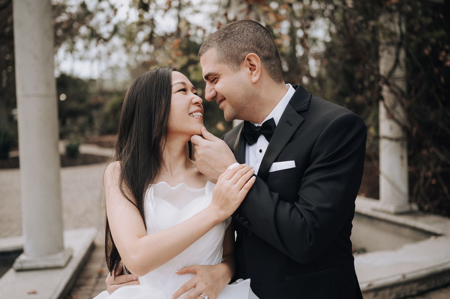 A romantic wedding couple shares an intimate moment outdoors near classical stone columns.