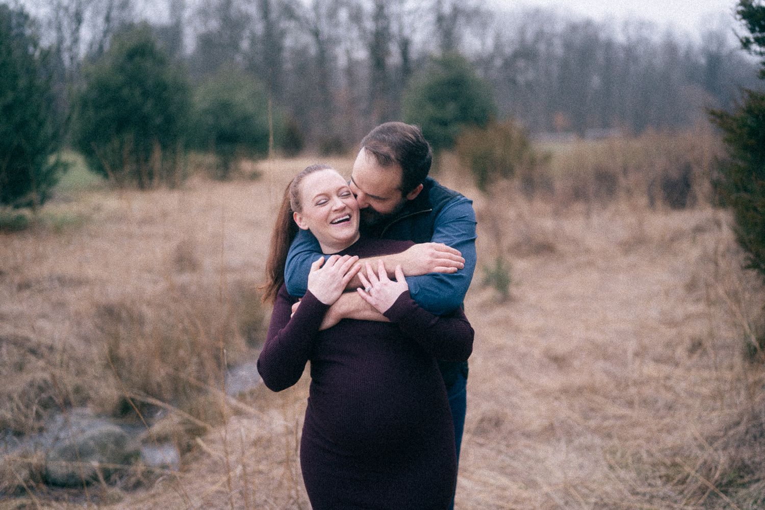 Emotional outdoor portrait showing embrace during pregnancy in winter landscape.