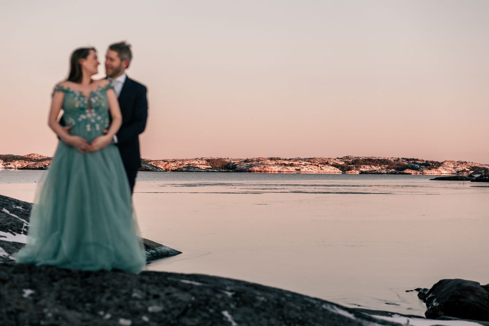 Elegant couple in formal wear embrace on snowy beach at sunset.